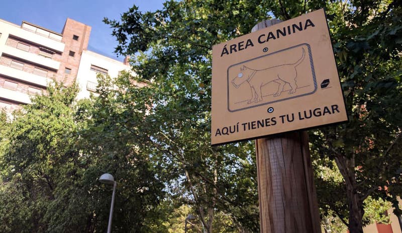A wooden sign in a Madrid park reading Area Canina, aqui tienes tu lugar, with a line drawing of a dog