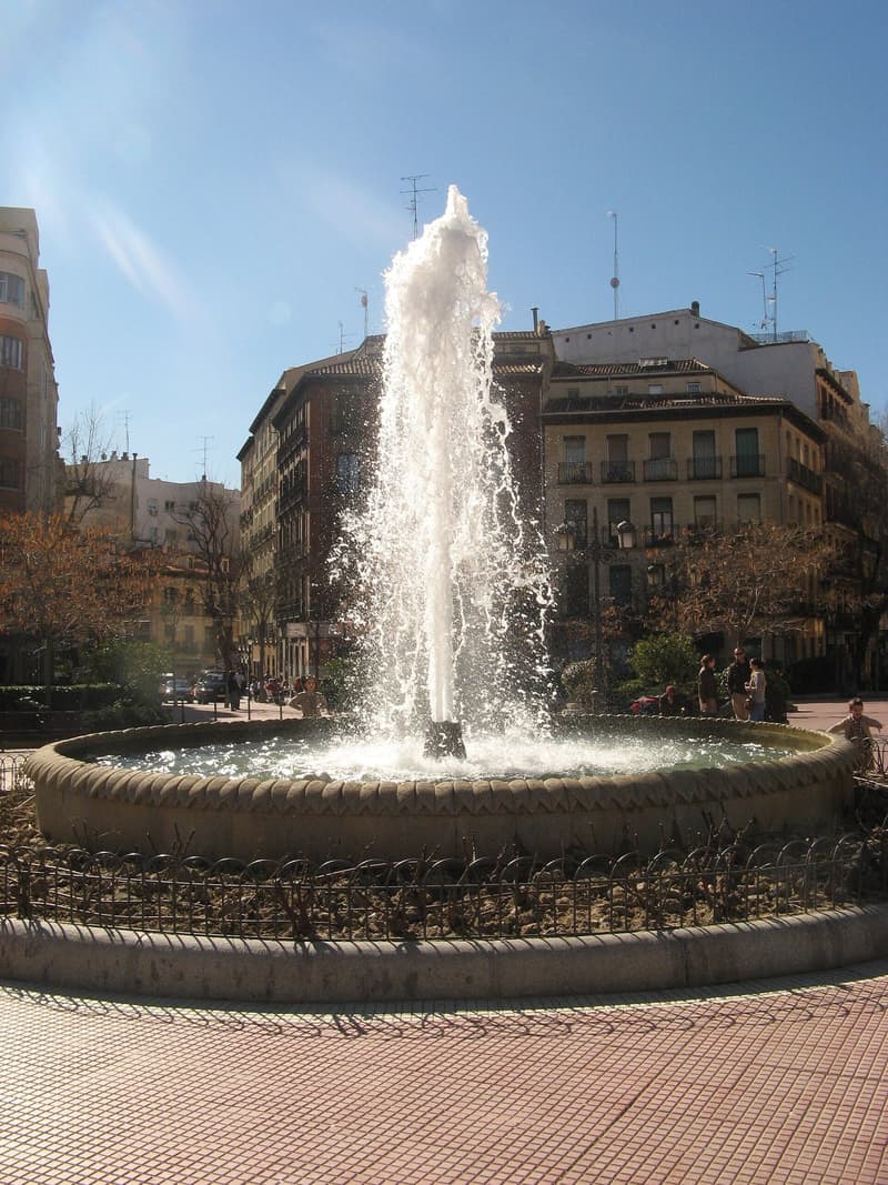 The fountain in Plaza de Olavide, Chamberi, Madrid, surrounded by trees and terrace tables